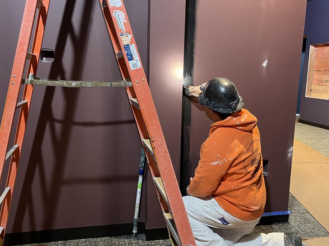 Worker paints wall trim in Museum gallery, March 18, 2026
