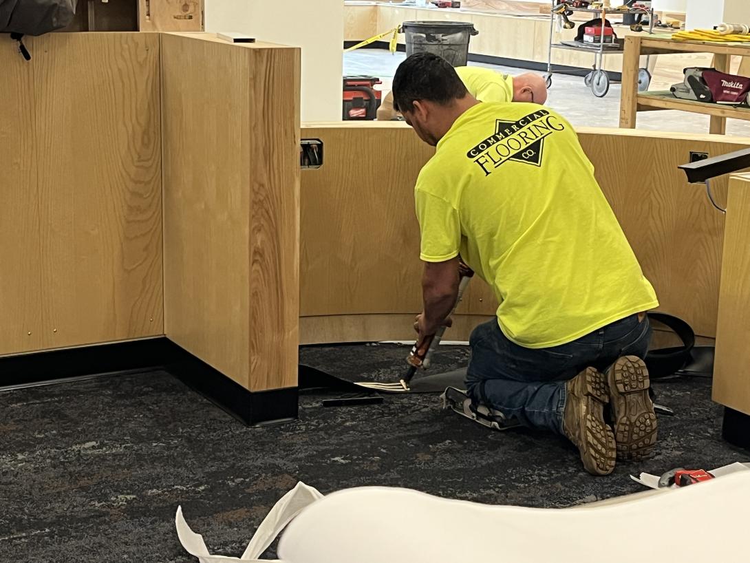 Worker attaches adhesive to baseboard trim inside the new reception desk, April 15, 2026