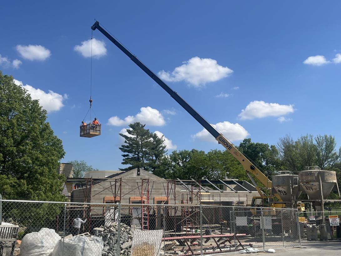 Workers in a basket being lifted by a crane to demolish the chimney, May 14, 2025